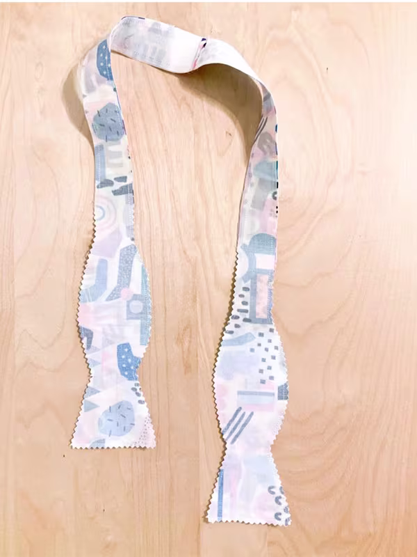 A bowtie sewn together, designs sides facing on a wooden surface.