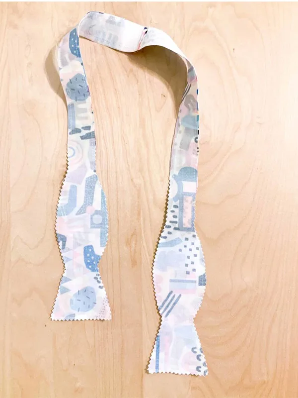 A bowtie sewn together, designs sides facing on a wooden surface.