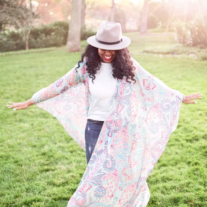 Person standing outdoors with arms outstretched, wearing a long, lightweight garment with a pastel paisley pattern.
