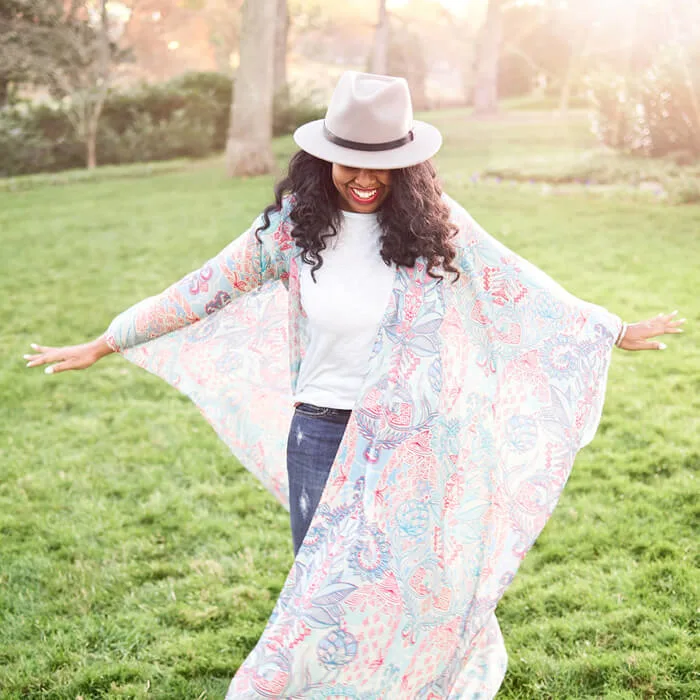 Person standing outdoors with arms outstretched, wearing a long, lightweight garment with a pastel paisley pattern.