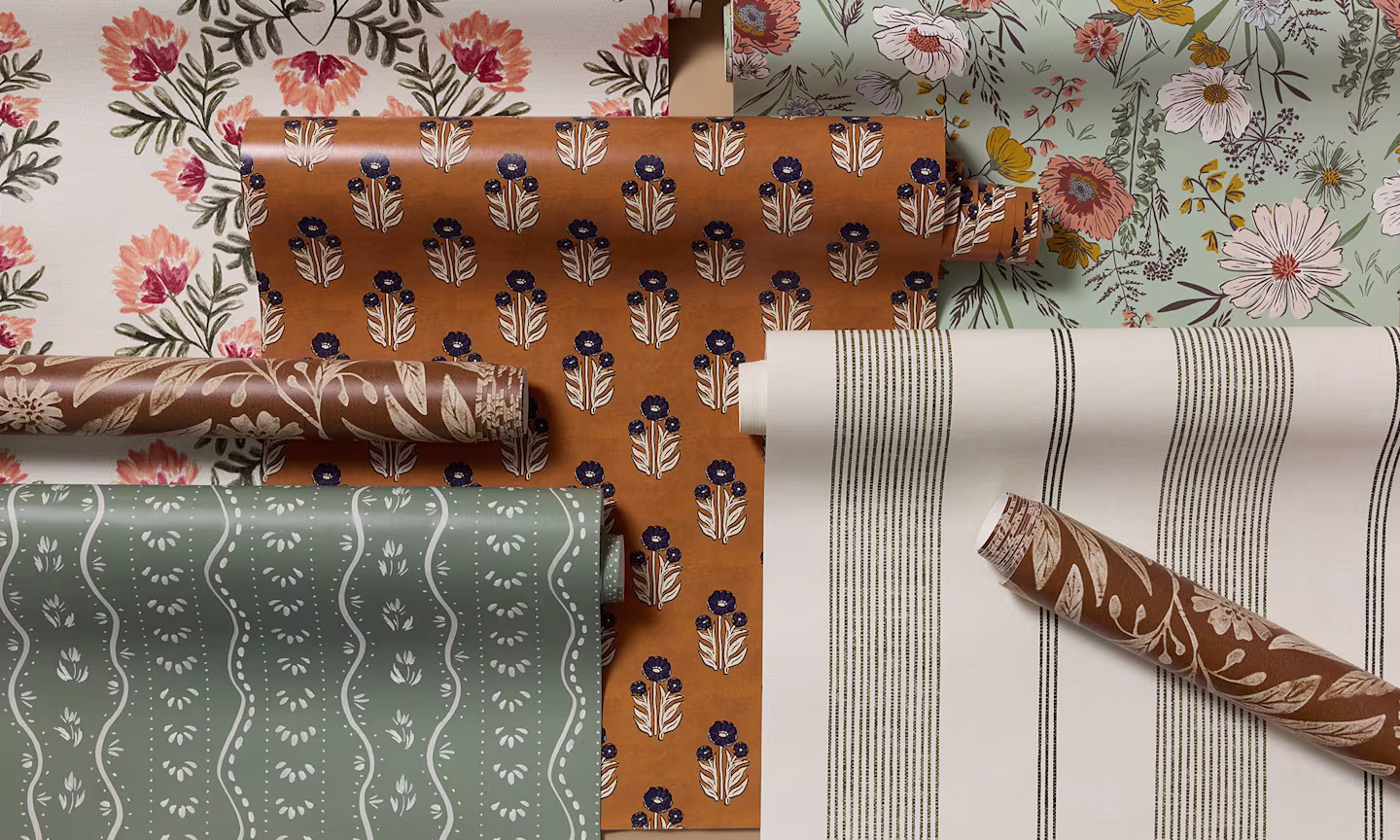 A curated assortment of wallpaper rolls featuring floral motifs, delicate botanicals, classic stripes, and folk-inspired patterns.