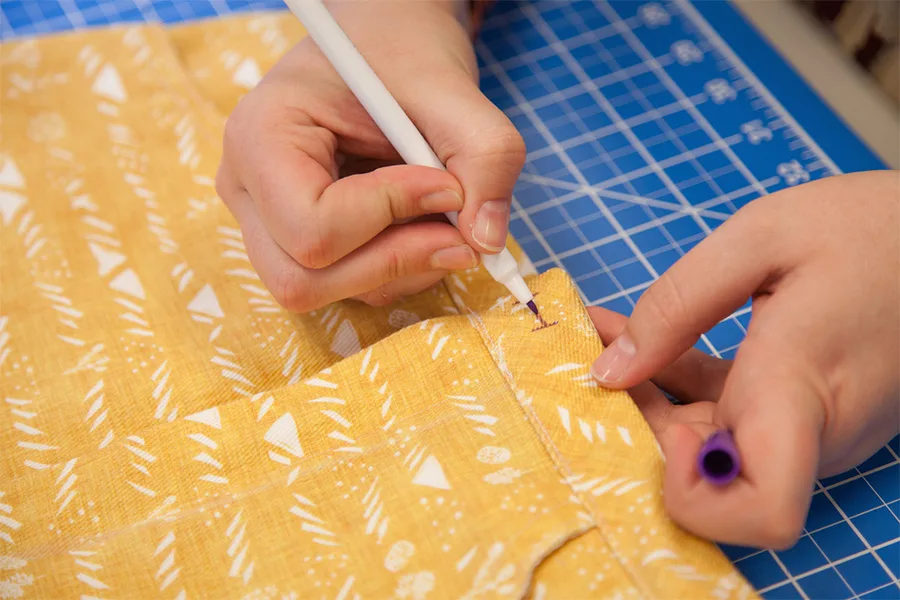 A close up of MaryAshlyn using a fabric marker to mark where her button hole will be on her skirt.