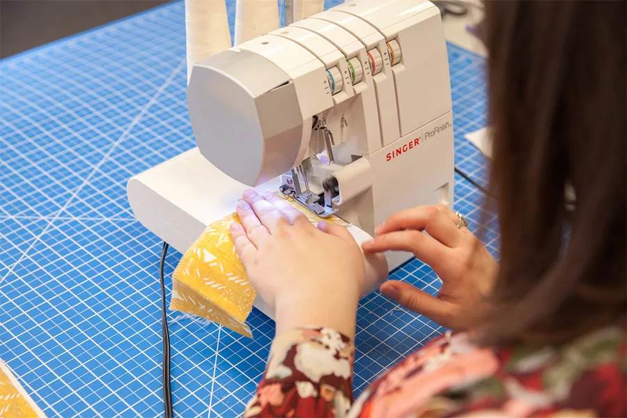 An over the sholder shot of MaryAshlynn finishing the edges of her fabric with a sewing machine.