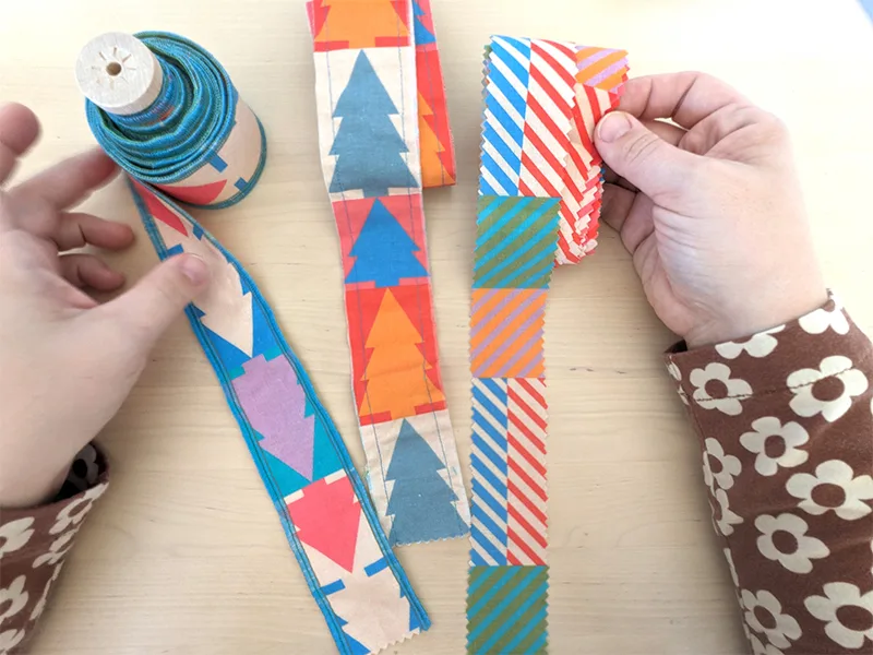Examples of three different fabric ribbon. The two left-hand ribbons are made with a design featuring jewel-tone and white Christmas trees. The ribbon on the right has a design with small squares of coordinating colors in varying pairings, also in jewel-t