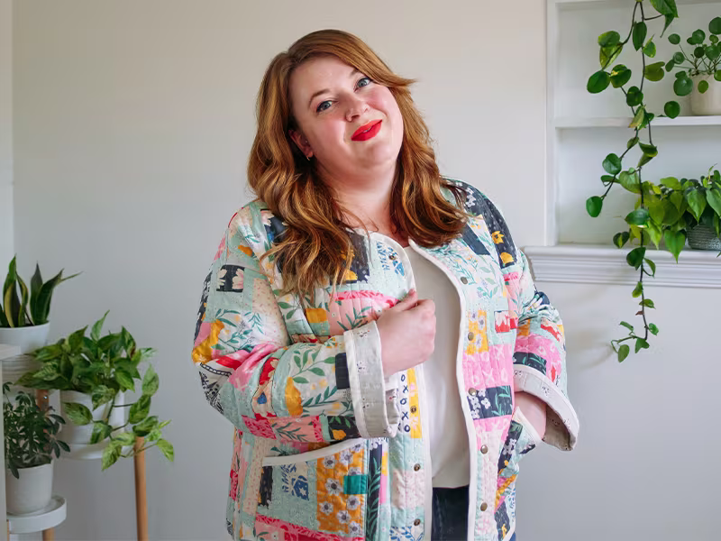 A close up of Meg's cheater quilt quilted jacket featuring delicate florals, most with a blue or pink theme. She is standing in front of a white wall.