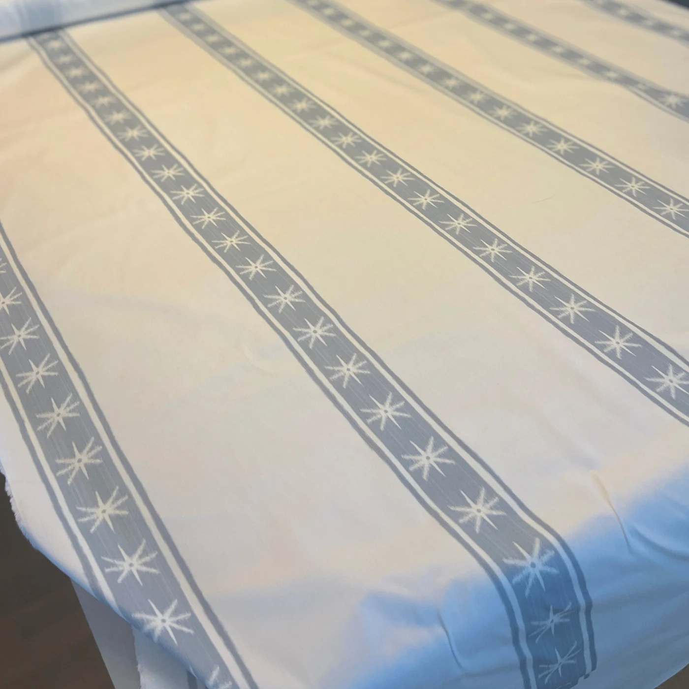 A close up of white fabric with vertical thick blue stripes with white stars. A thin blue stripe appears on either side of each thicker stripe.