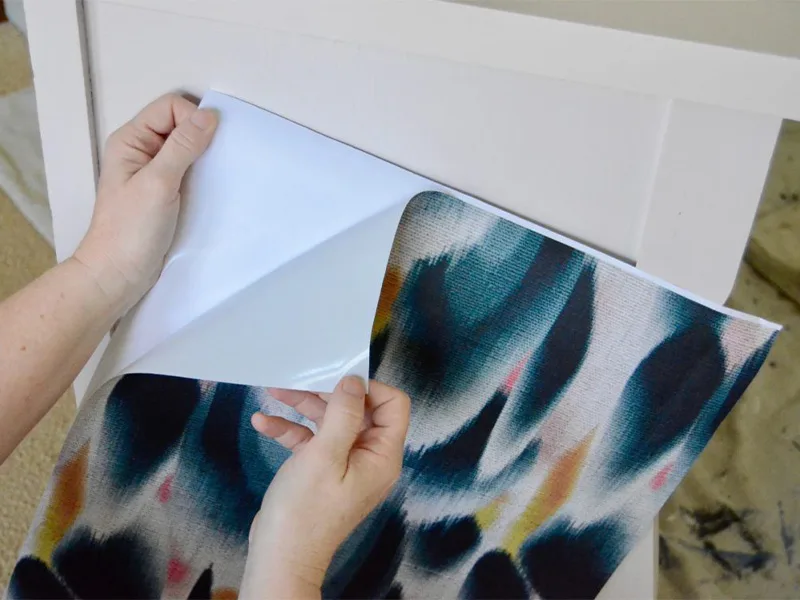 Barb removing the paper backing from the wallpaper in order to attach it to the dresser.