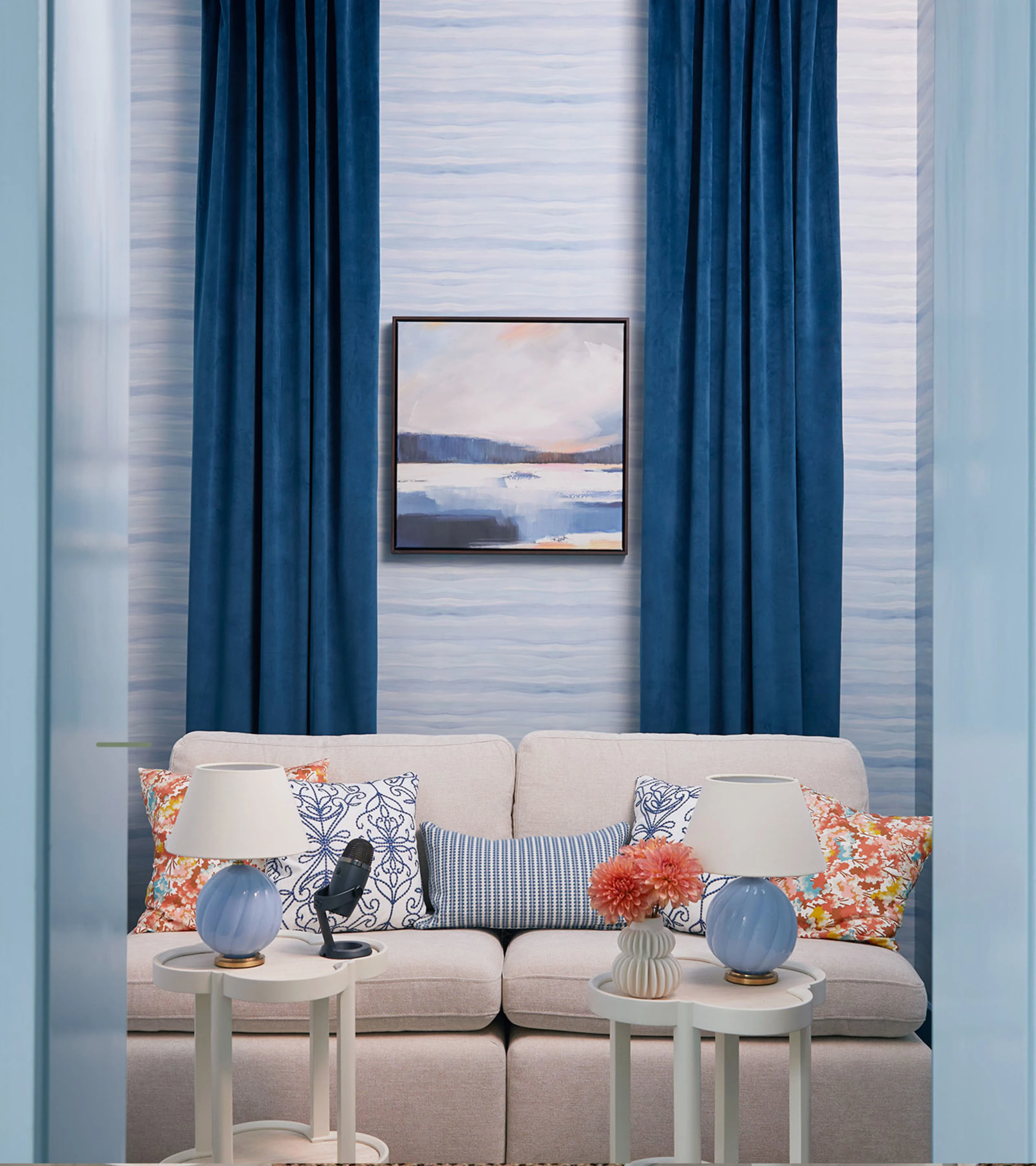 A media room with a couch, side tables, pillows, and behind blue watercolor wallpaper.