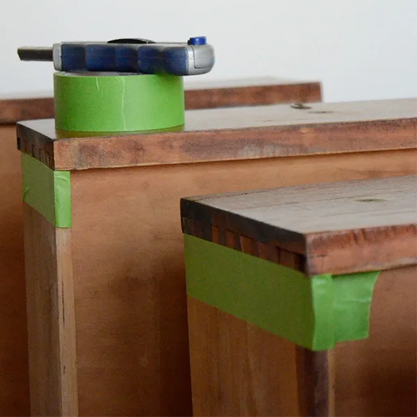 Three drawers standing up. The sides are taped with green painters tape. The rolls sits on top of one of the drawers along with a craft knife.