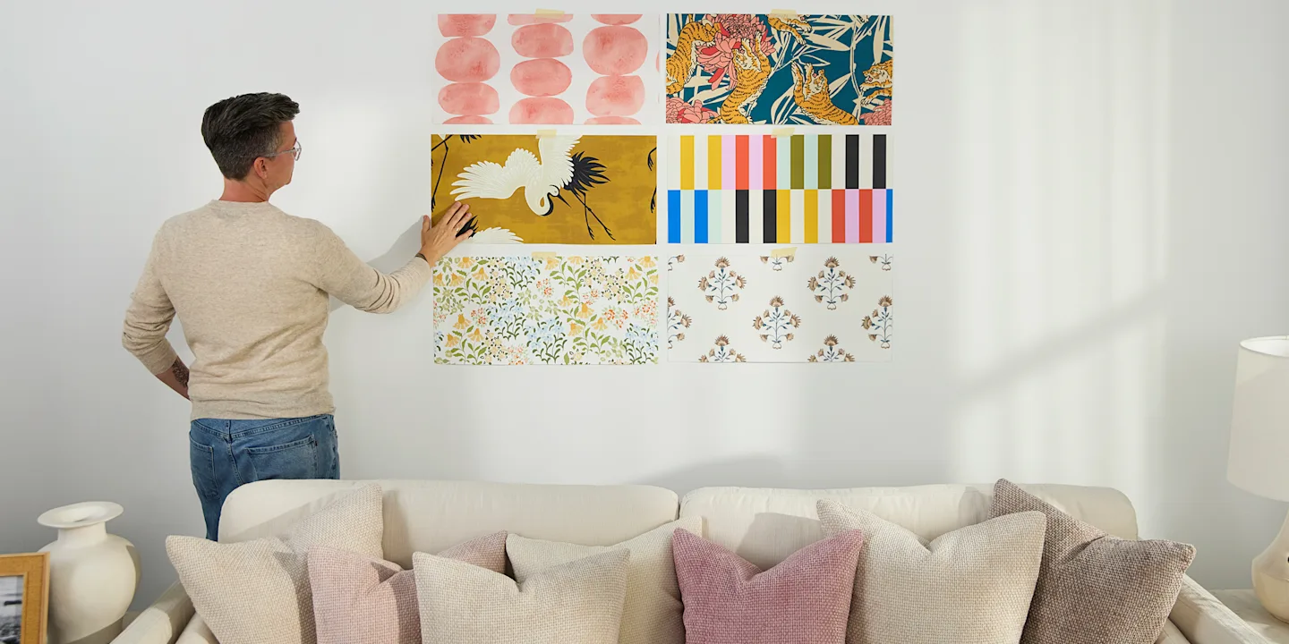 Person assessing wallpaper samples on a wall.
