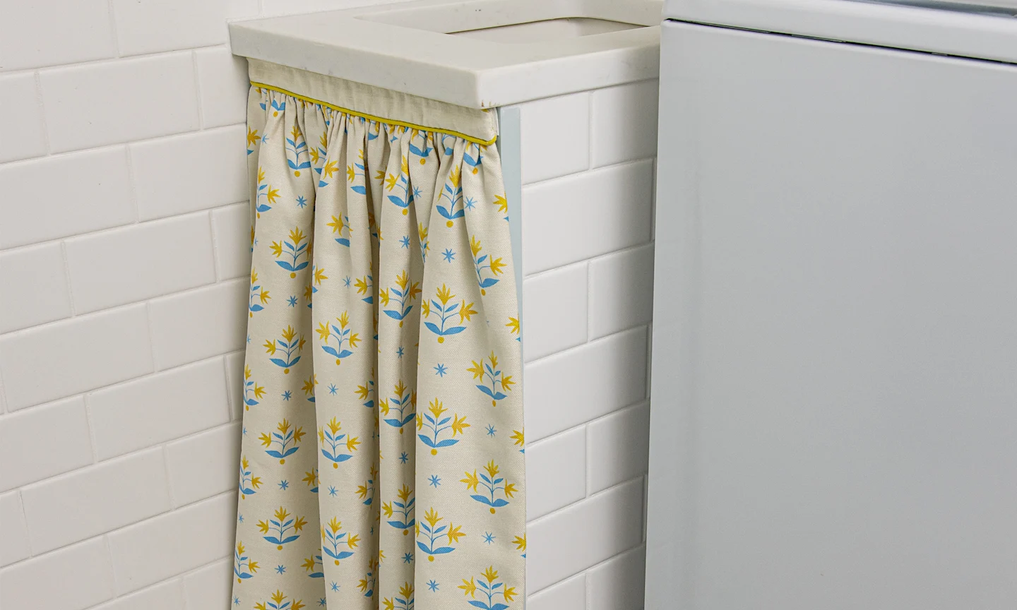 A yellow block printed curtain hanging below a sing in a laundry room.
