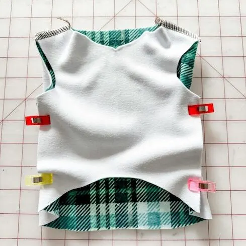 The front bodice piece lays design-side down on top of the back bodice piece, which is laying design side up. Two sewing clips hold the left and right sides of the fabric together. Two sewing clips have been placed at the top of the bodice pieces as well.