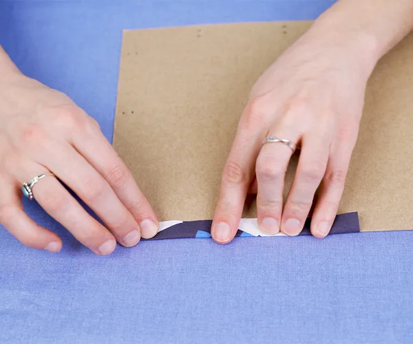 Folding a small section of a fabric over a piece of cardboard to create a seam. The cardboard is acting like a seam template.