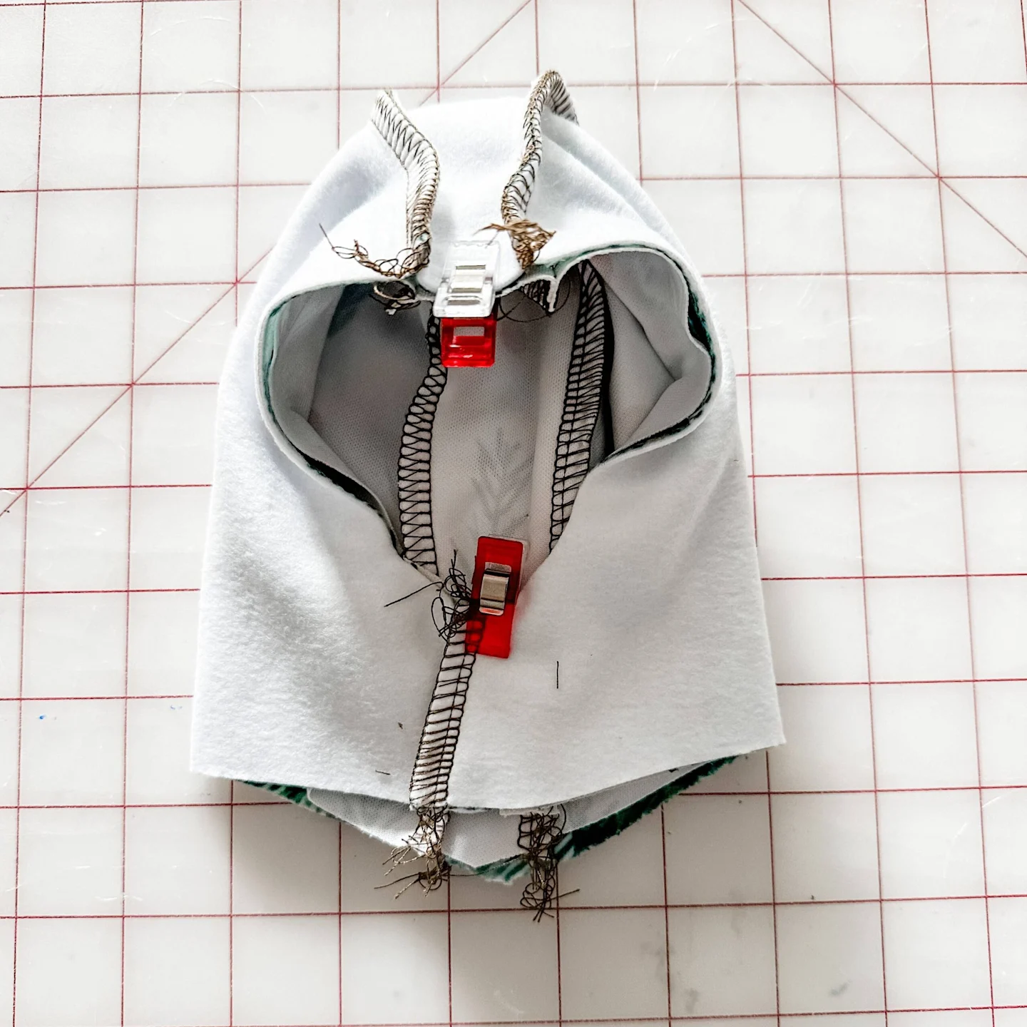 The exterior hoodie piece is turned design side in while the interior hoodie piece is turned design side out. The exterior hoodie piece is placed inside the interior hoodie piece. Sewing clips secure the two pieces at the center top and bottom where the d