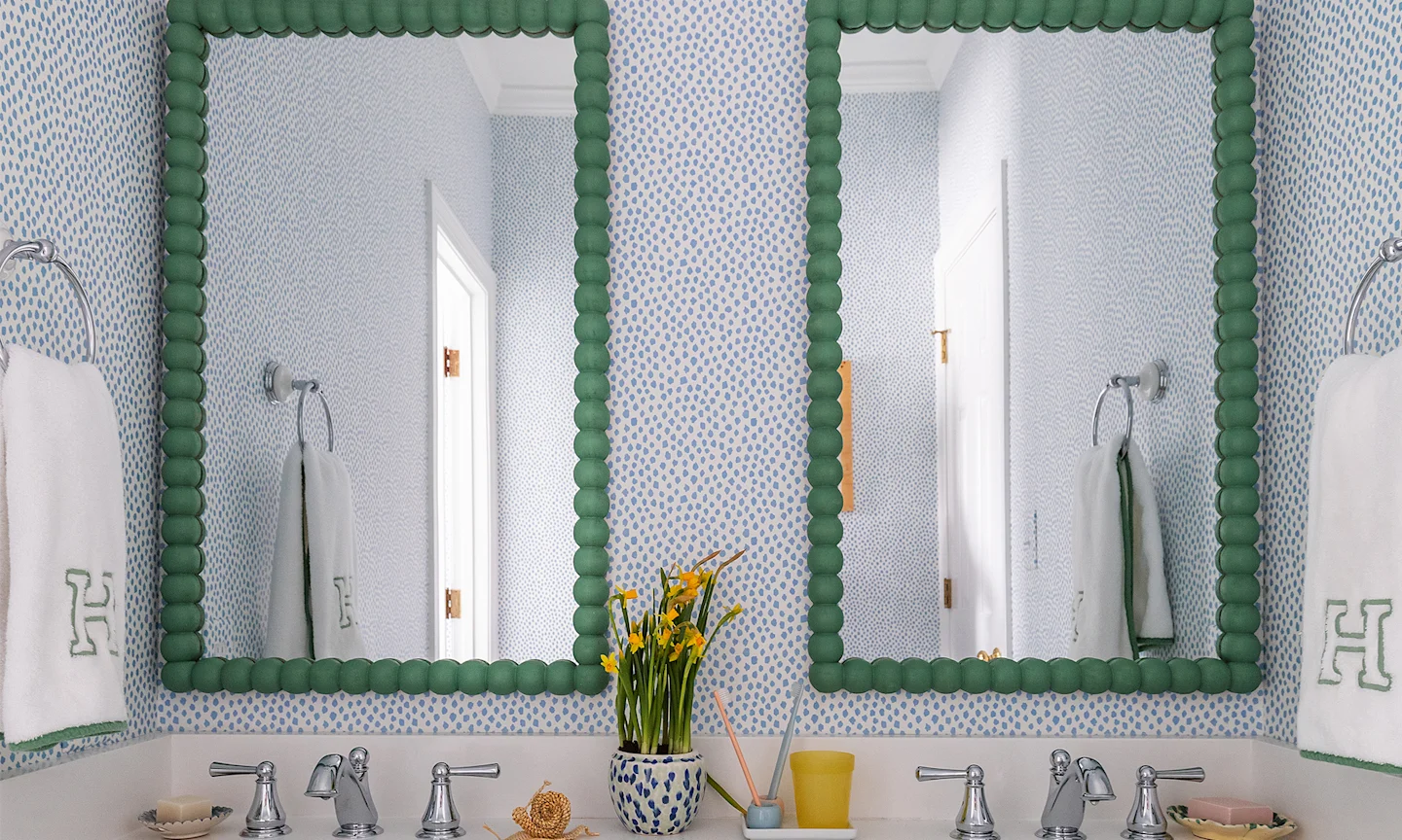 Bathroom with spotted blue wallpaper and green mirrors.