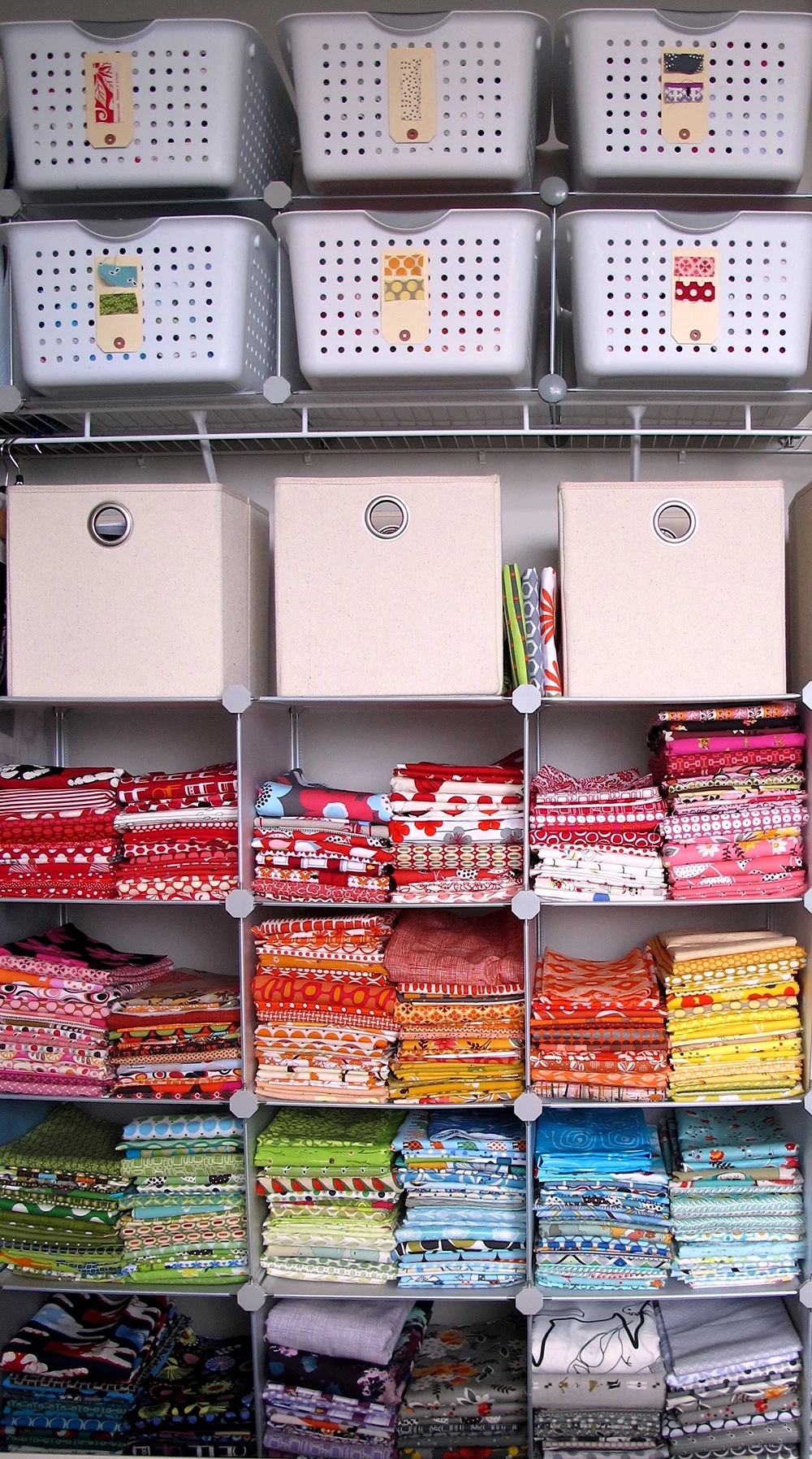 a closet storage organizer with baskets organized by row and stacks of fabric organized by color