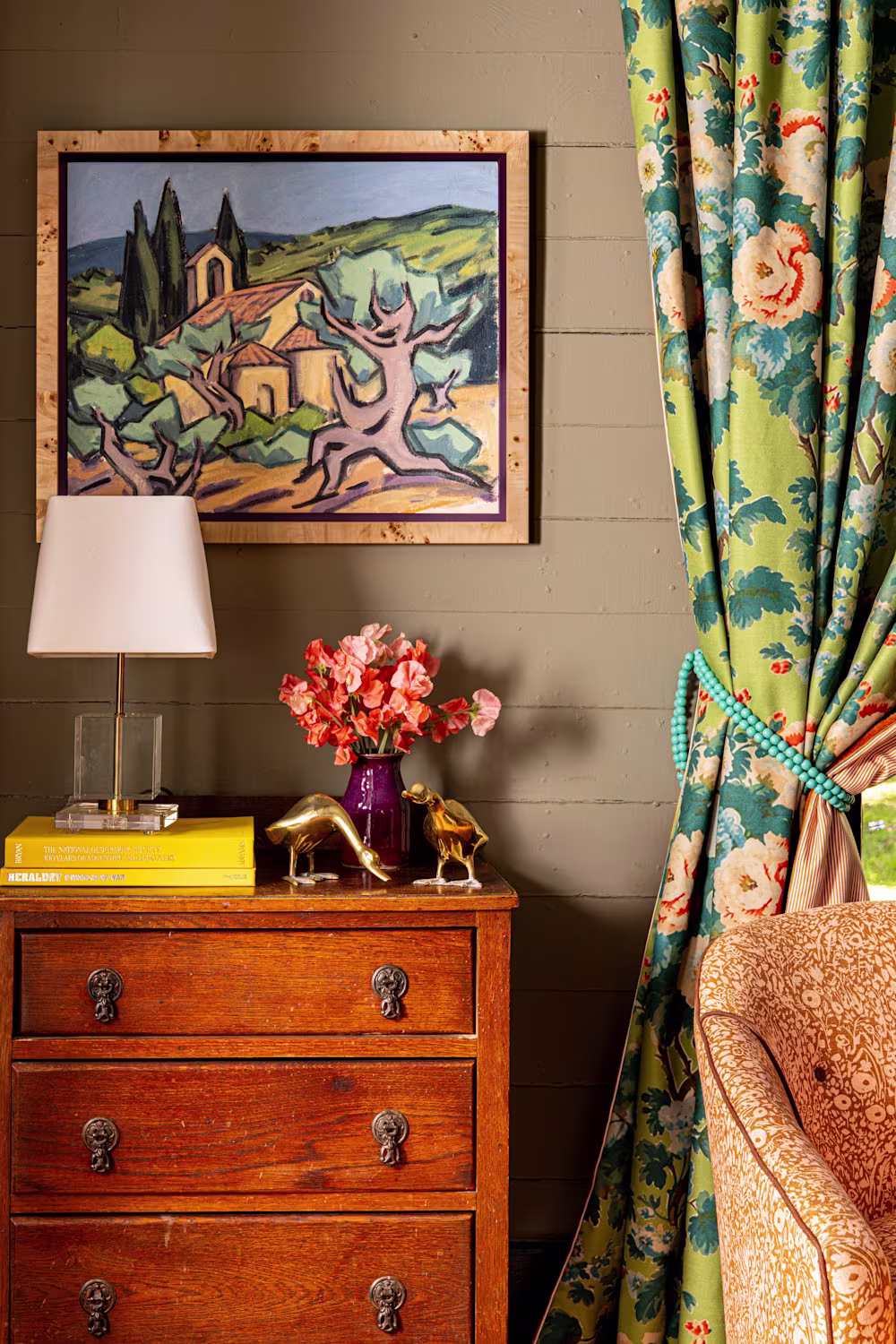 Vintage bedroom corner with floral curtains, wood dresser, and framed artwork.