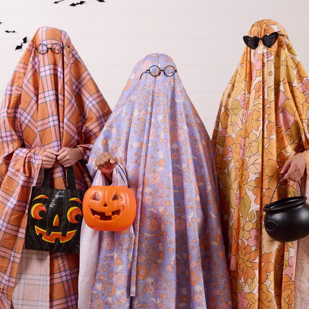 Three people wearing bold floral sheet ghost costumes