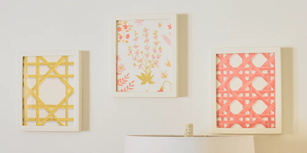 A close up of three of the framed wallpaper swatches, each swatch has been placed in a white frame. From left to right, the wallpaper designs are: a yellow trellis on a white background, small pink flowers with green leaves on a white background and a pin