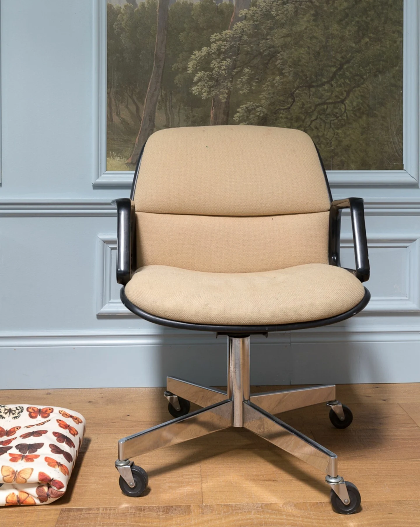 Image of a beige drop-seat chair in front of a light blue wall and on a light wooden floor.