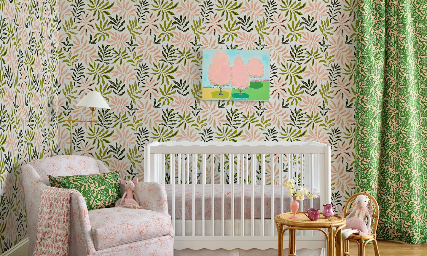 Nursery with pink and green tropical botanical wallpaper and coordinating curtains, decor and upholstery.