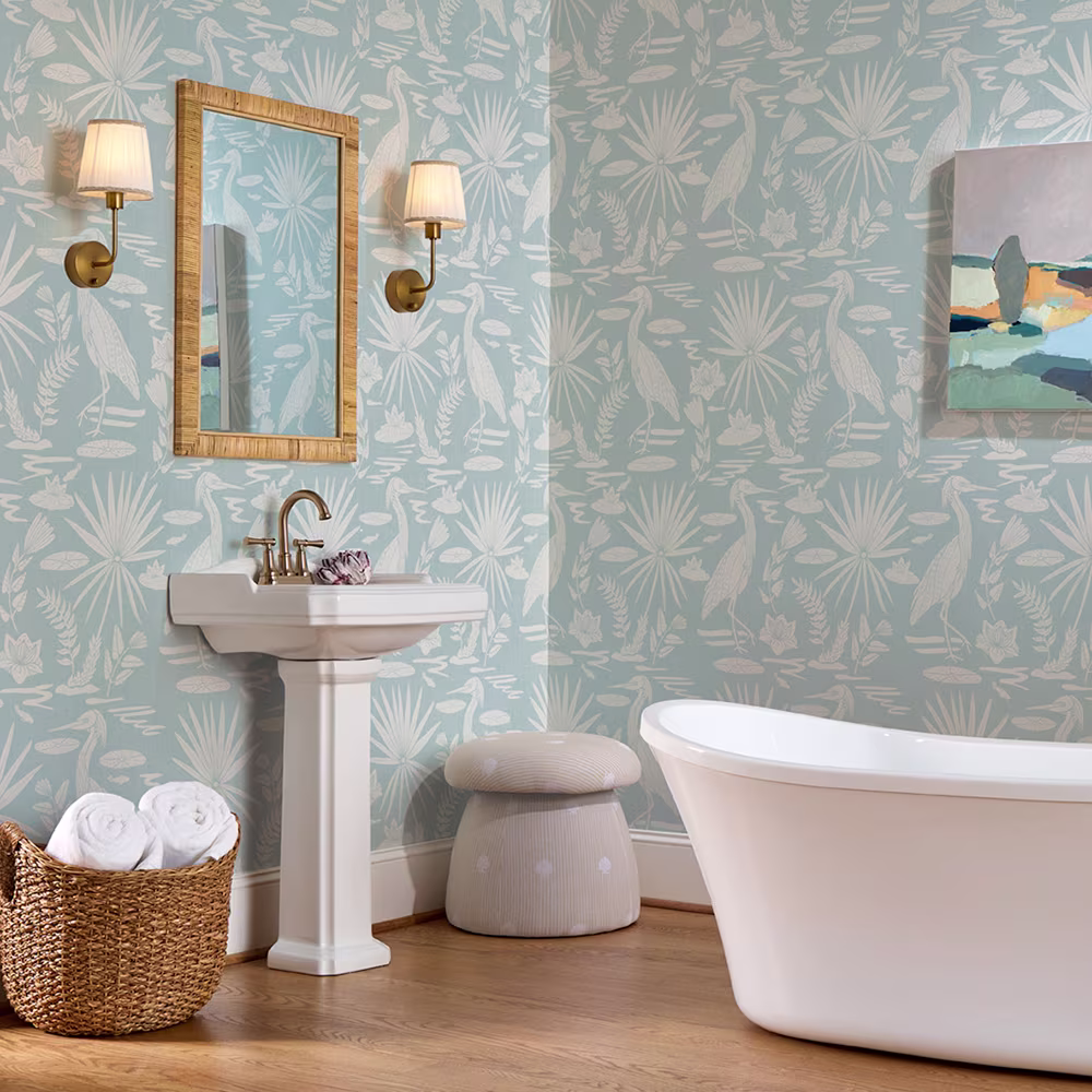 Bathroom with blue and cream coastal heron wallpaper a sink tun and ottoman with a tan striped shell design.