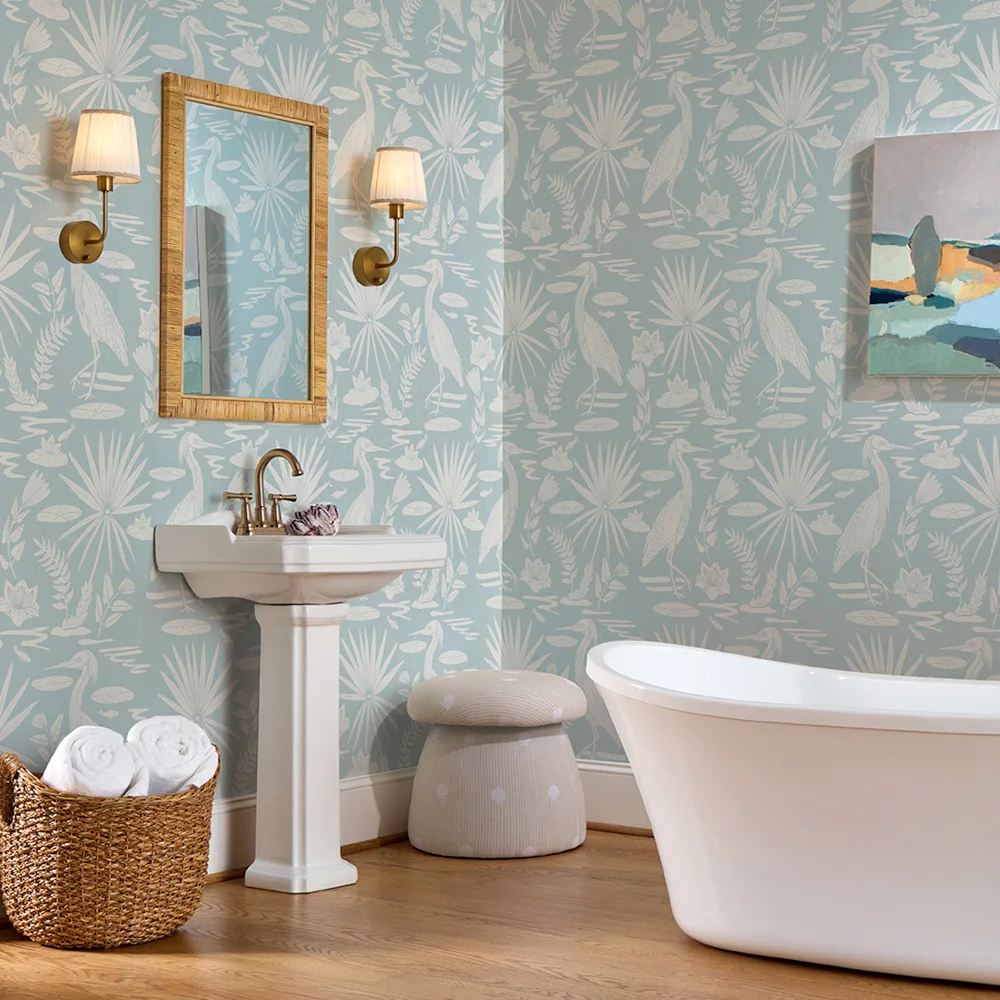 Bathroom with blue and cream coastal heron wallpaper a sink tun and ottoman with a tan striped shell design.