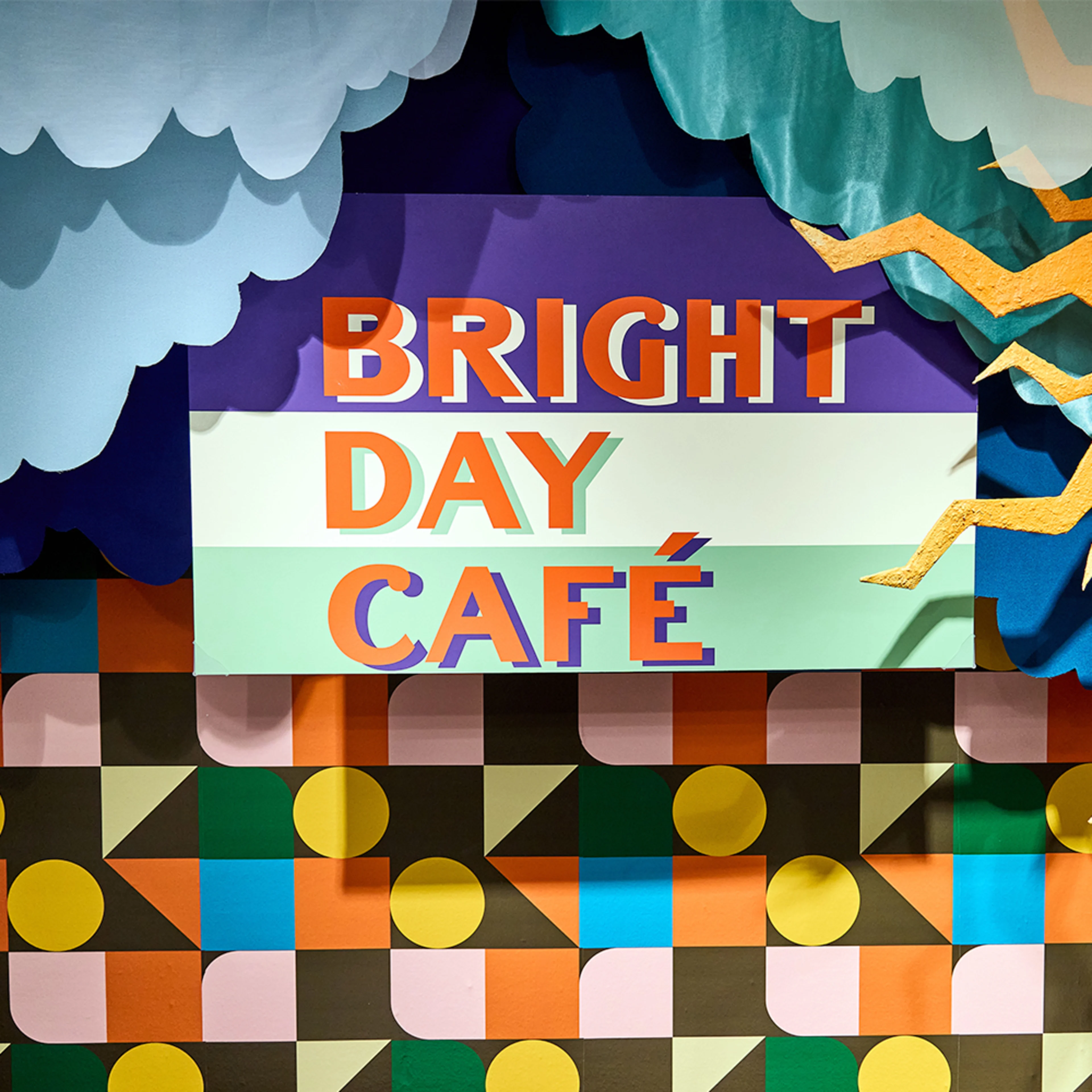 Bright Day Cafe sign with geometric Spoonflower wallpaper behind it at Neocon 2025.