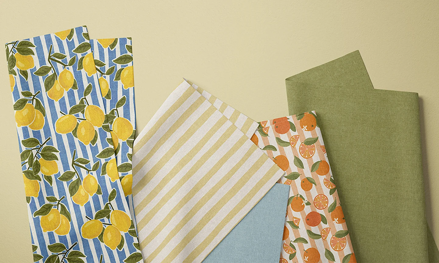 Summery fabrics striped and fruit patterned fabric fat quarters on a neutral background.
