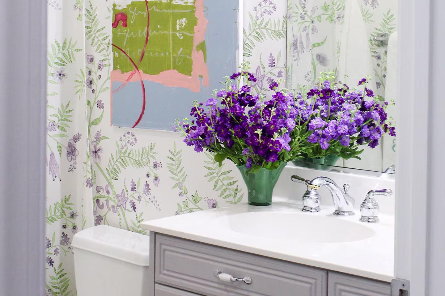 Bathroom with floral wallpaper and purple flowers in a vase.