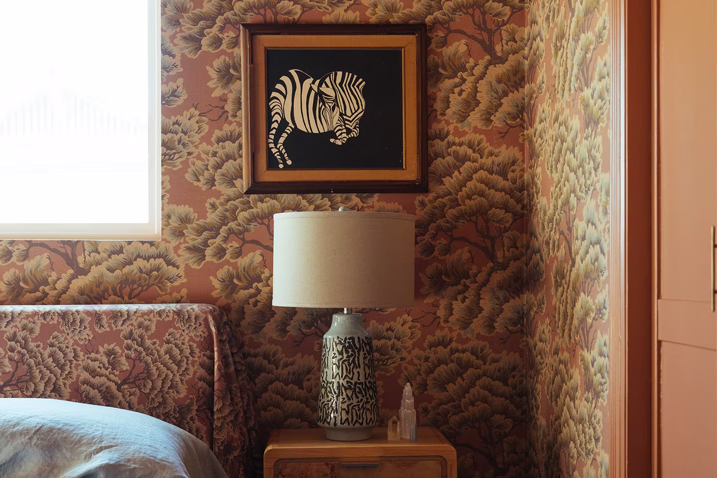 Earthy bedroom with pattern drenched wallpaper and matching fabric headboard.