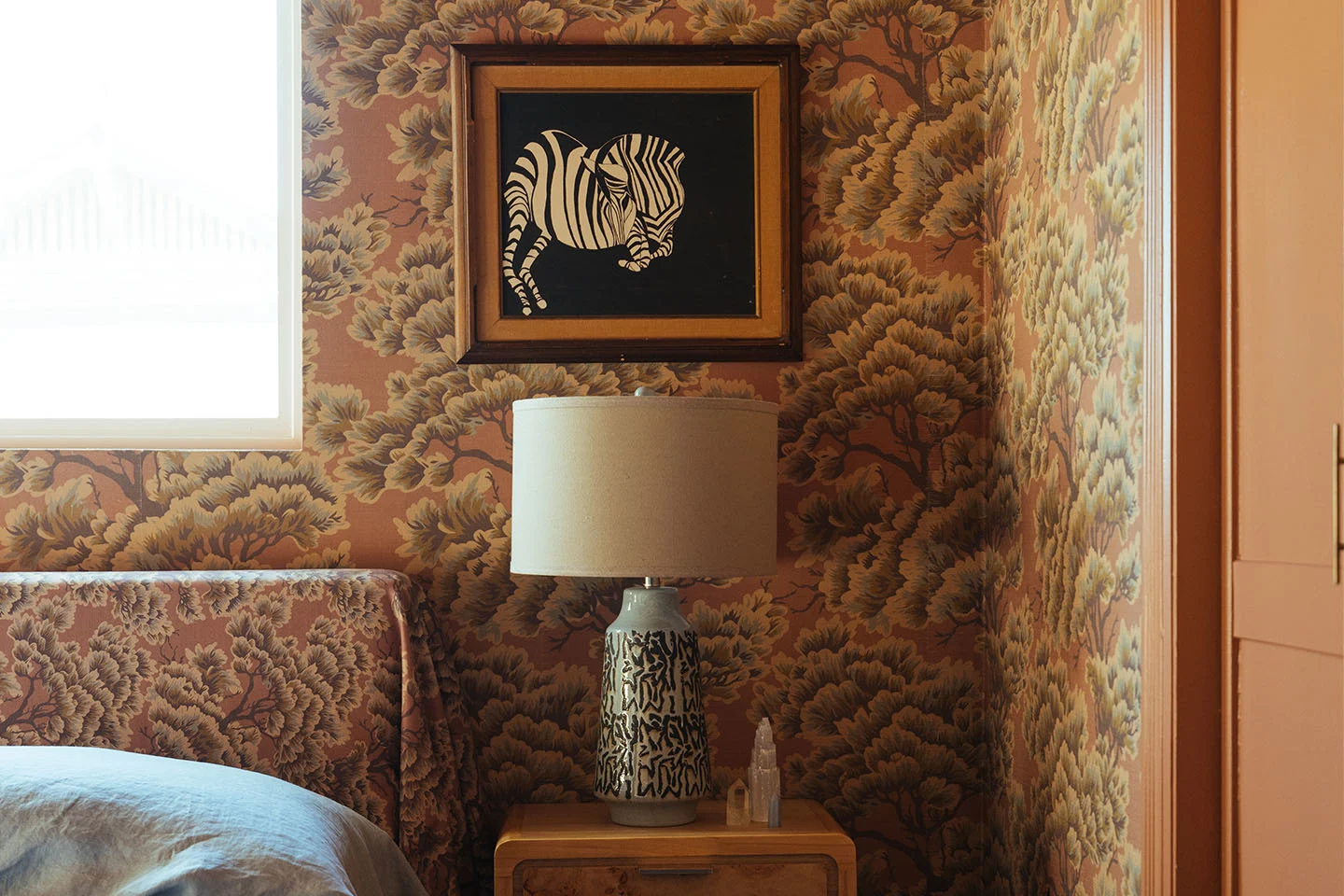 Earthy bedroom with pattern drenched wallpaper and matching fabric headboard.