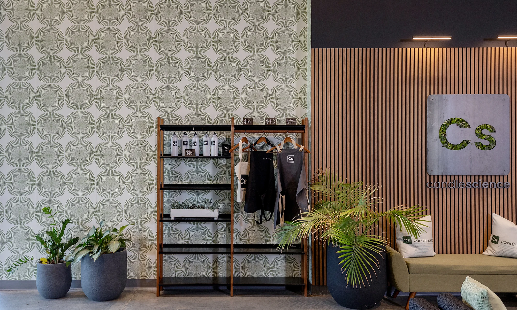 Candle Science office space with a shelf, plants and couch with green geometric wallpaper.