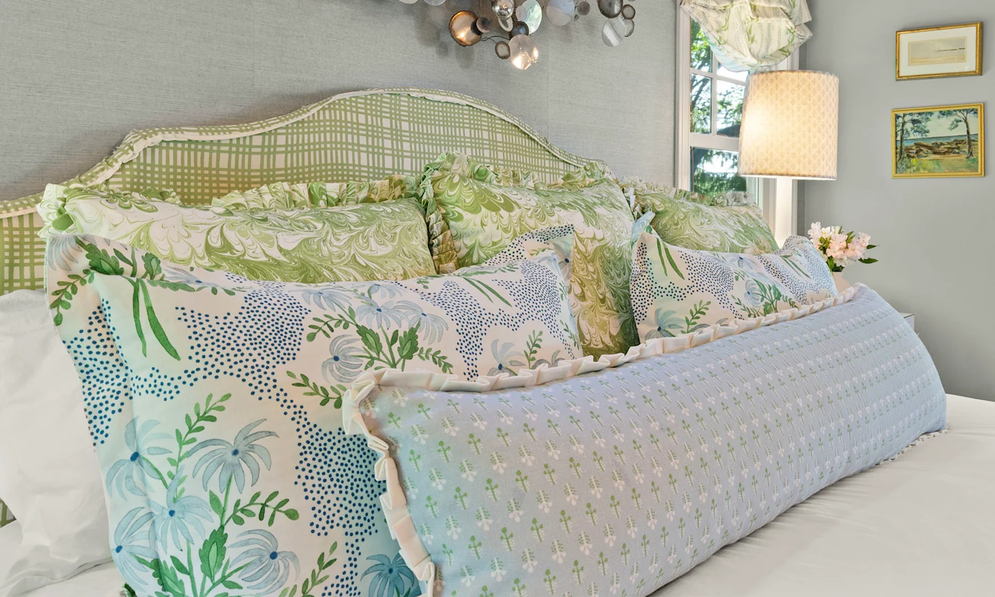 Bed with green and blue floral pillows and upholstered headboard.