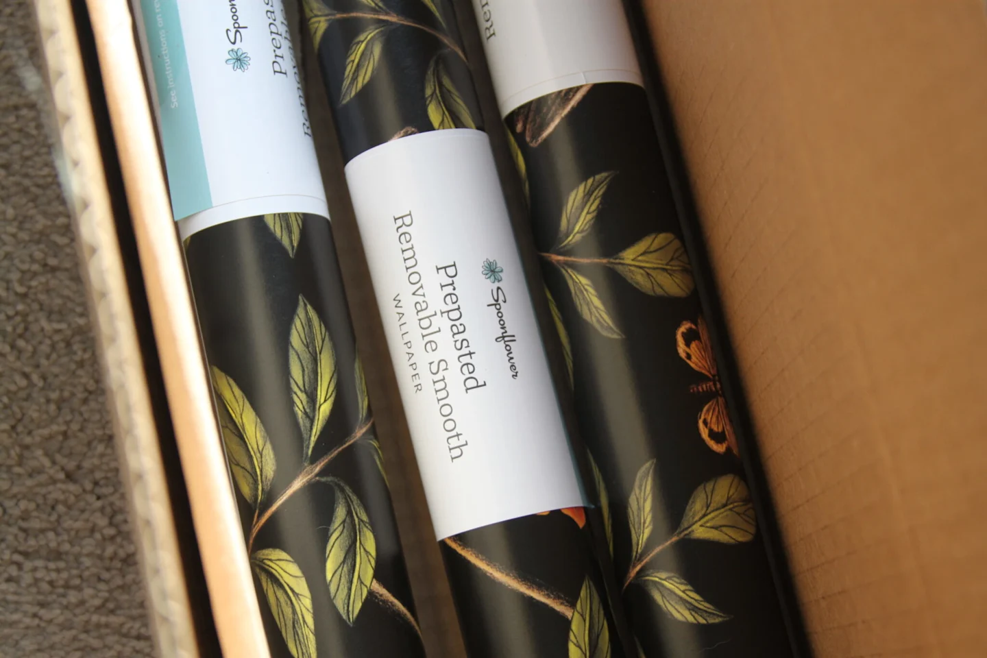Rolls of black wallpaper featuring deep green leaves