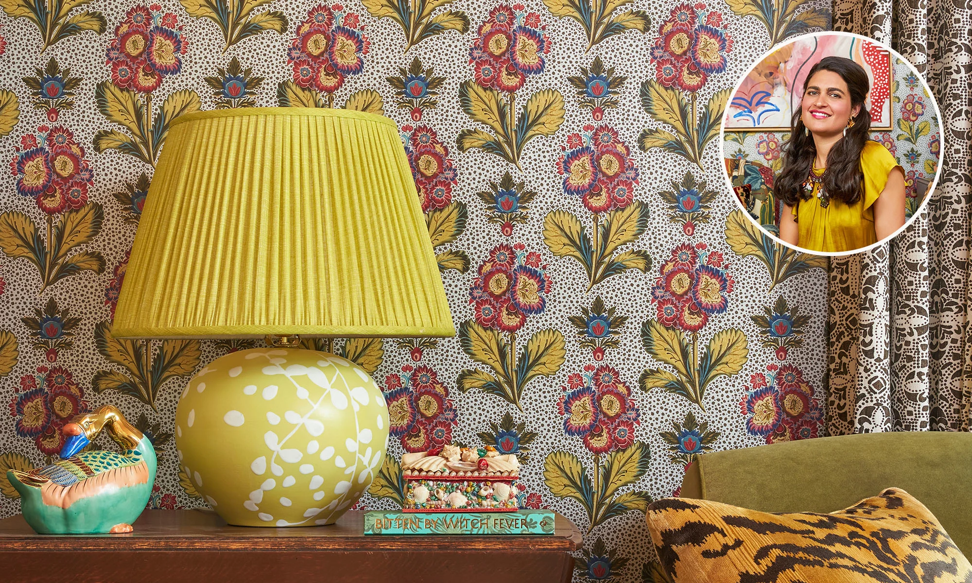 Floral silver wallpaper, with a side table, green couch, pillow, and a yellow lamp.
