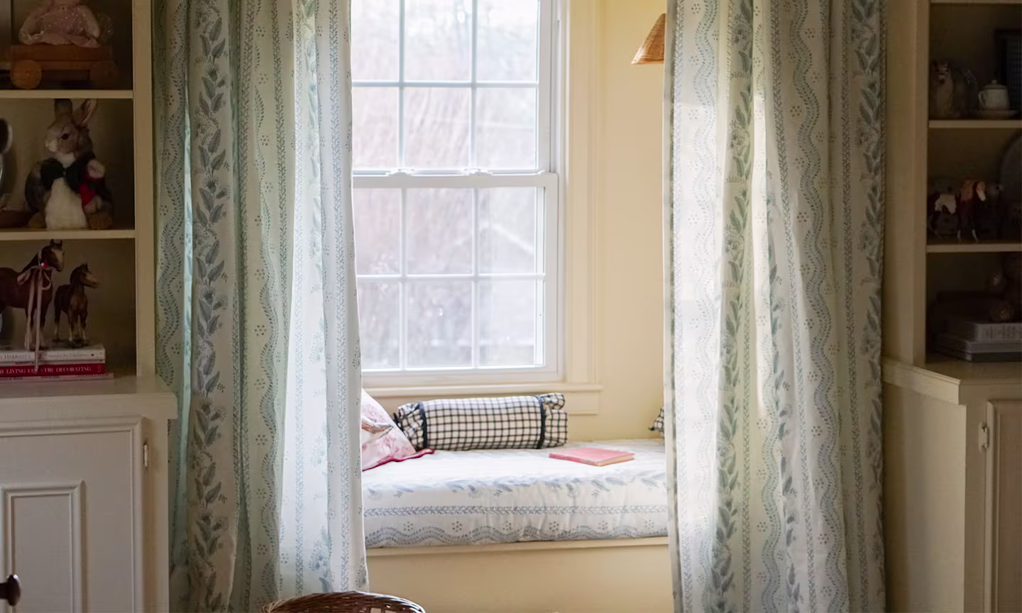Window seat with cushion upholstered in a blue floral stripe fabric with matching curtains.