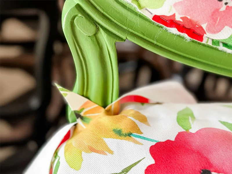 A close up of the back leg of the settee with fabric around it. The fabric is cut in a V shape with one piece pointing upward. The other piece is hanging from the edge of the leg.