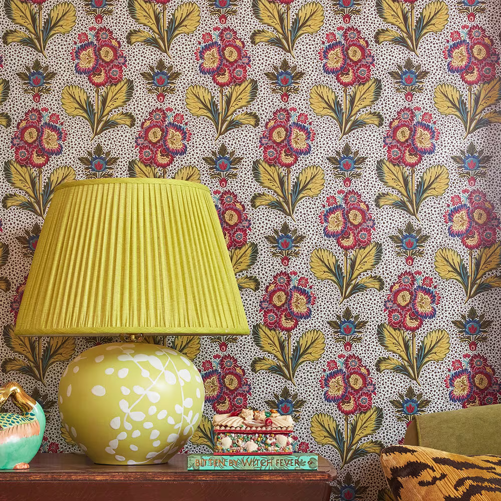 A lamp on a side table behind silver metallic floral wallpaper.