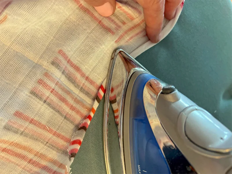 Close up of the caftan double folded neckline being pressed with an iron.