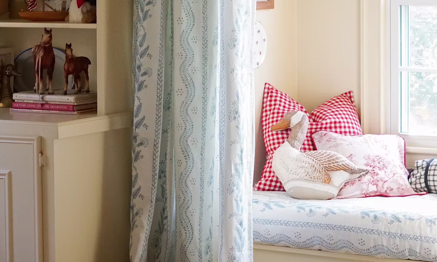 Window seat with cushion upholstered in a blue floral stripe fabric with matching curtains.