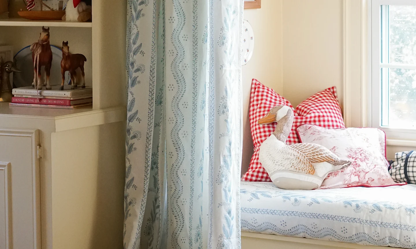 Window seat with cushion upholstered in a blue floral stripe fabric with matching curtains.