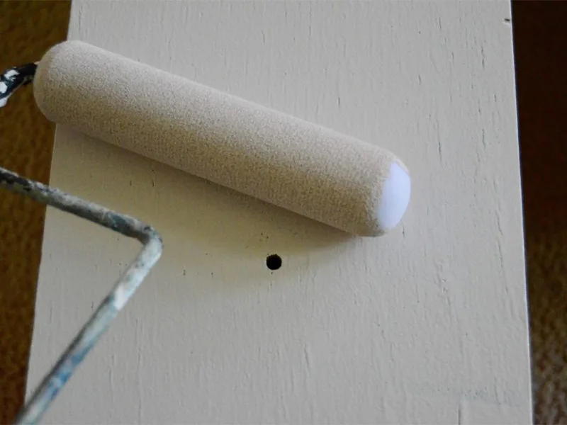 A paint roller layers on a painted dresser drawer.