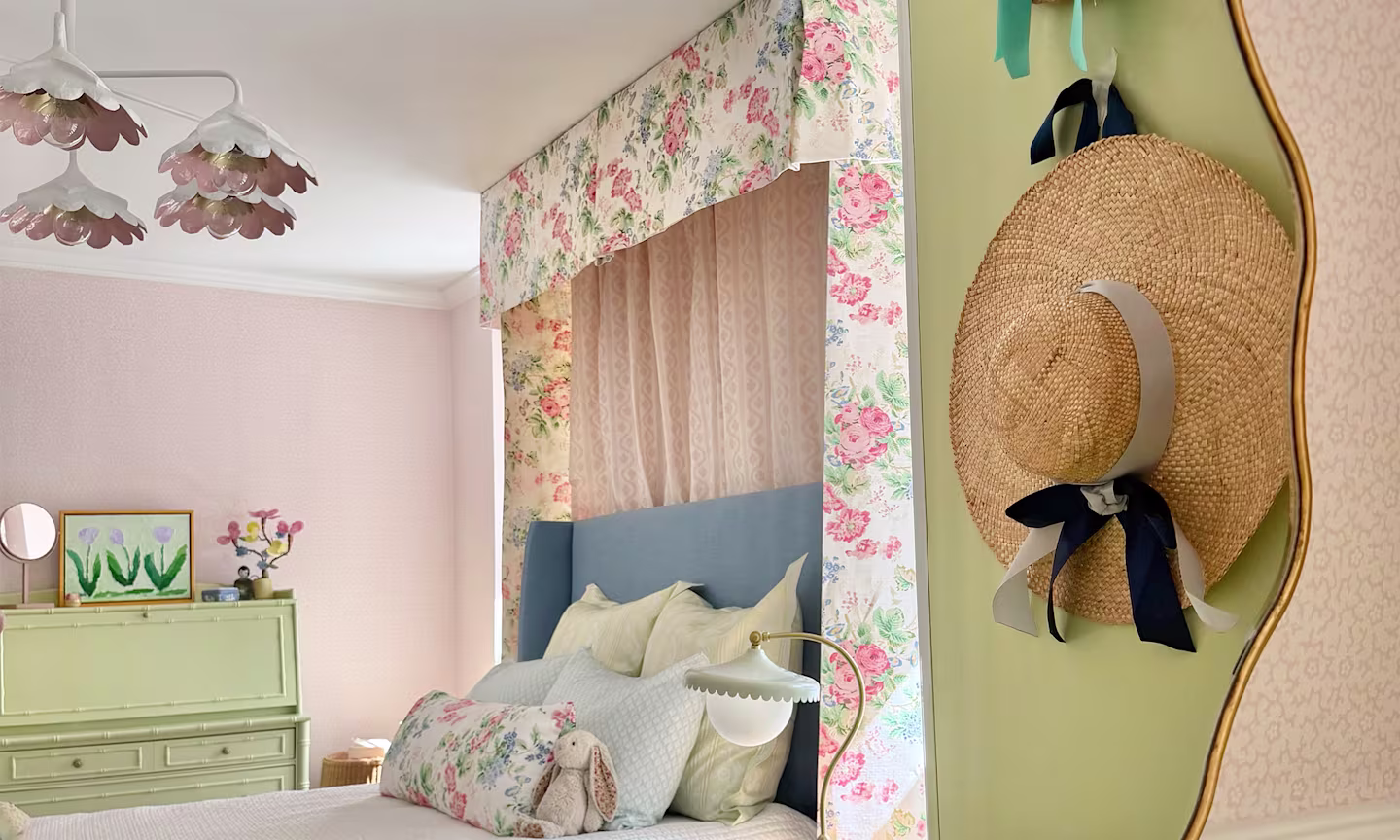 Girls bedroom with pink wallpaper a floral chintz bed canopy and coordinating pillows on the bed.