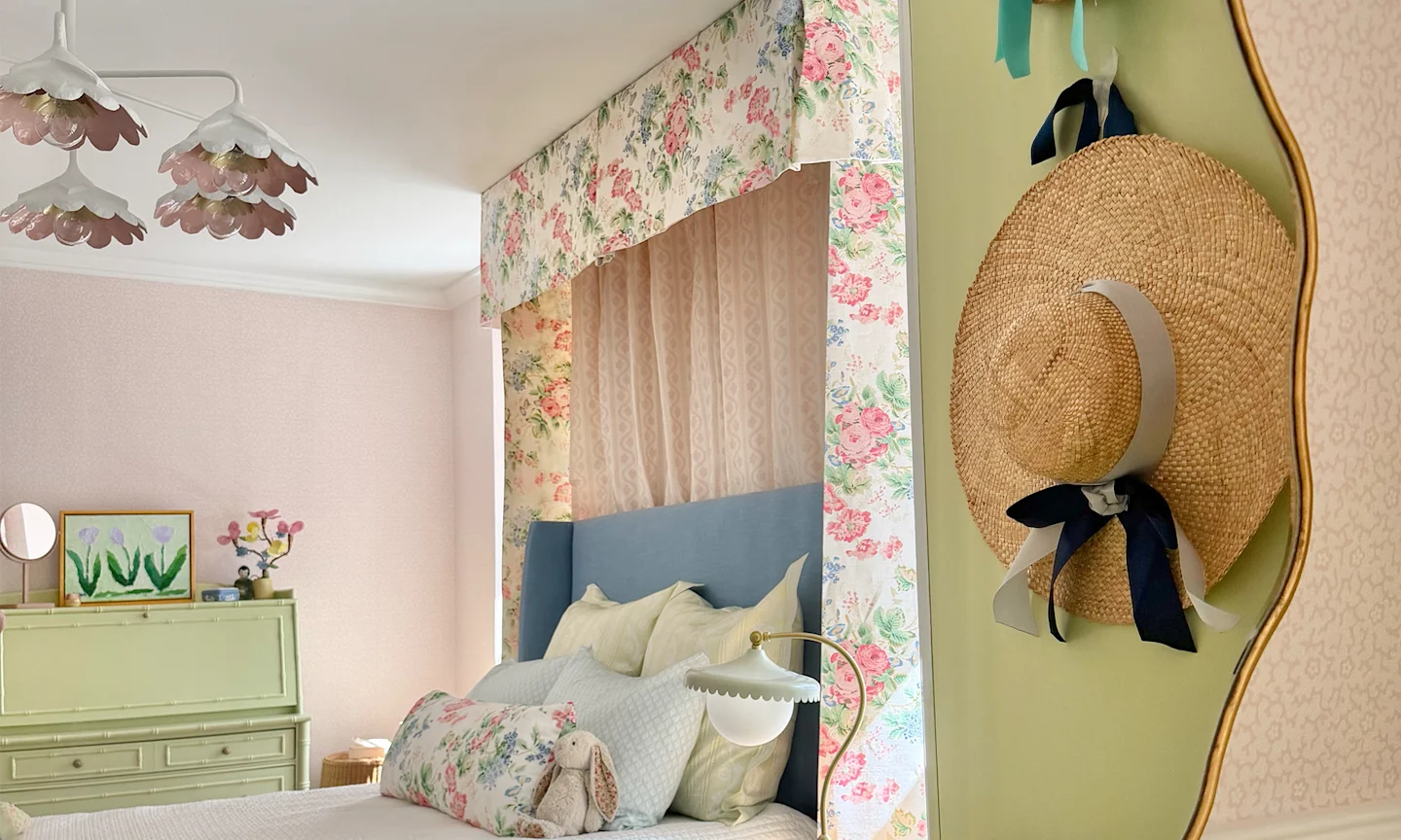 Girls bedroom with pink wallpaper a floral chintz bed canopy and coordinating pillows on the bed.