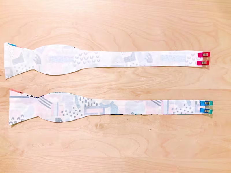 Four bow tie pieces are clipped together design sides facing on a wooden surface.