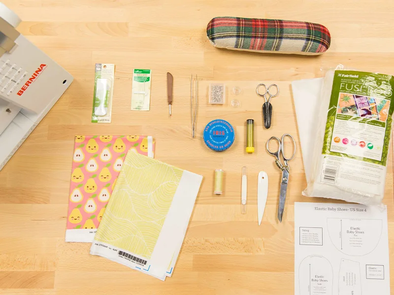 Materials to make baby shoes lay on a wooden surface.