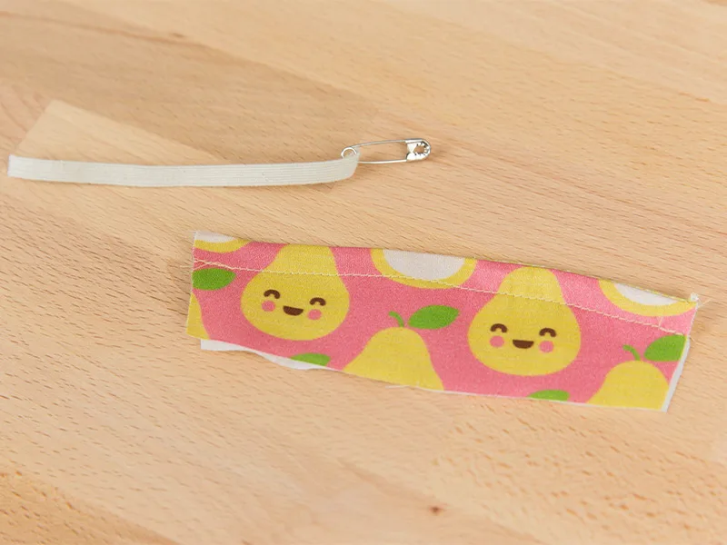 A piece of elastic with a safety pin on the end is near a piece of fabric with an elastic casing.