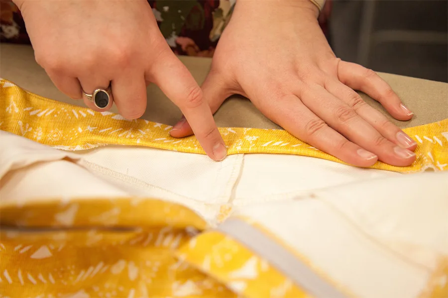 A close up of MaryAshlyns fingers holding down the waistband as she folds the raw edges under to stitch them inside the skirt.