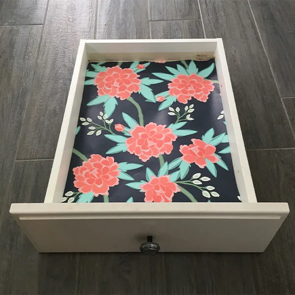 A drawer is on the floor with floral wallpaper in its base.